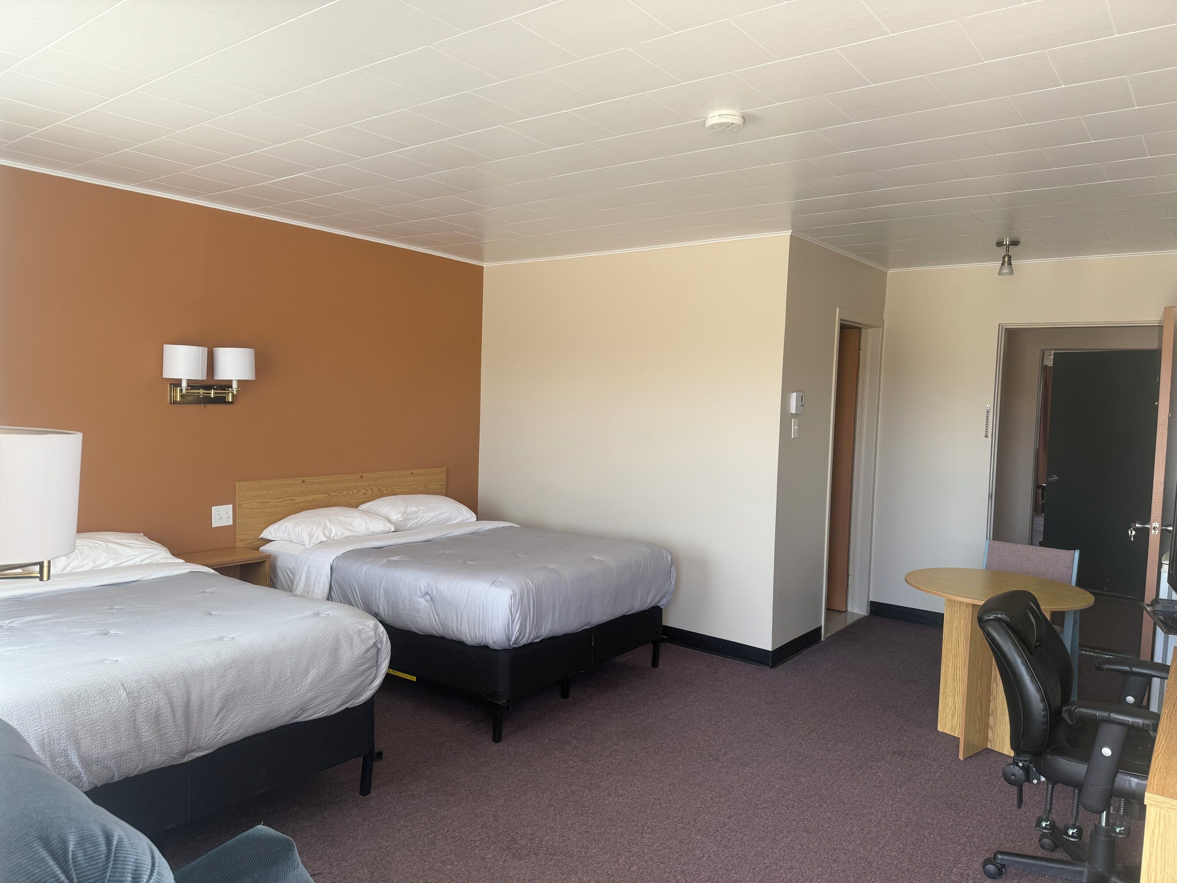 A hotel room with two beds, a desk, a chair, and a small table.