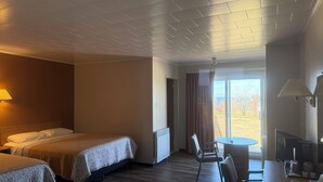 Habitación de hotel con dos camas, una mesa de comedor, sillas, televisor y vistas al exterior.