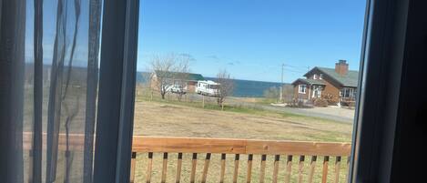 A view from a window with a wooden deck, overlooking a grassy area with a house and a white vehicle.
