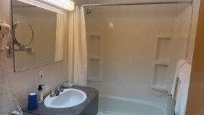 Un baño con lavamanos, espejo, ducha y toallero.