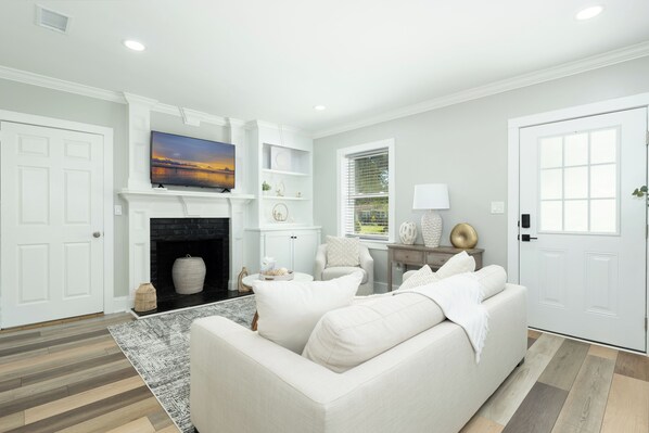 A living room with a fireplace, white sofas, a TV, and a window with blinds.