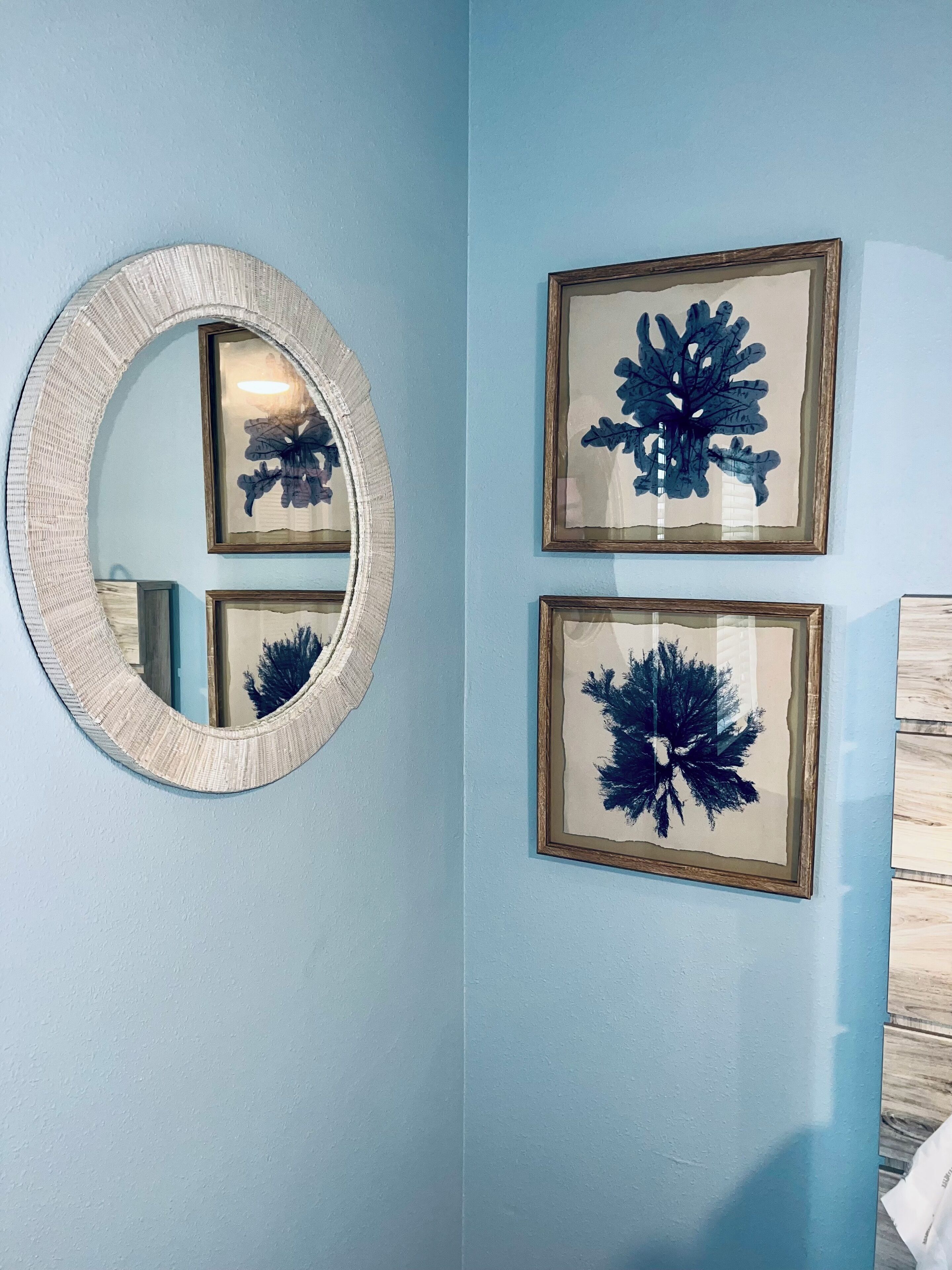 A wall with a round mirror and two framed botanical prints.