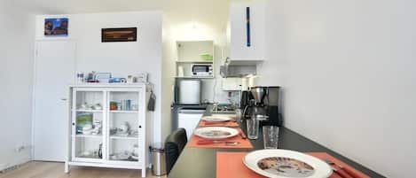 Une cuisine compacte équipée d’un four à micro-ondes, d’une machine à café et d’une table à manger pour deux personnes.