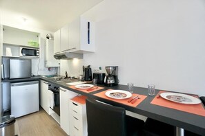 A compact kitchen with a microwave, stove, and coffee maker. There are two chairs and a table set for two.