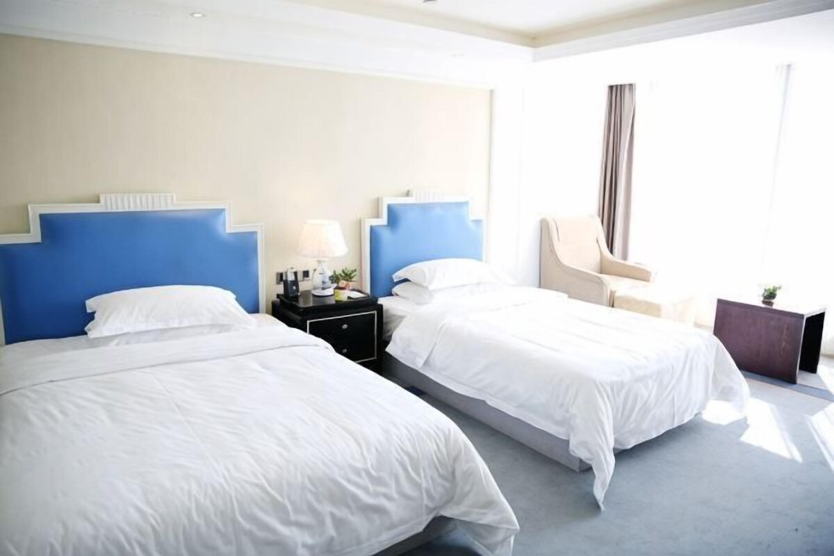 A hotel room with two beds, a desk, a chair, and a window with curtains.