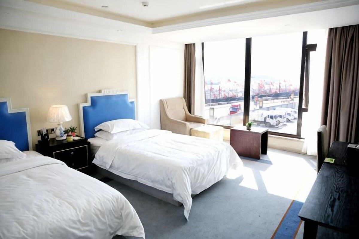Een hotelkamer met twee bedden, een bureau, een stoel en een groot raam met uitzicht.