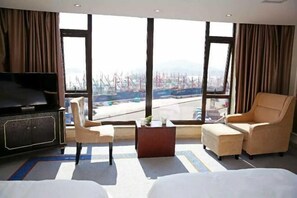 A hotel room with a large window, a television, a sofa, a chair, and a small table.