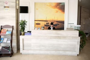 A reception desk with a painting of boats on water, a TV, and a plant.