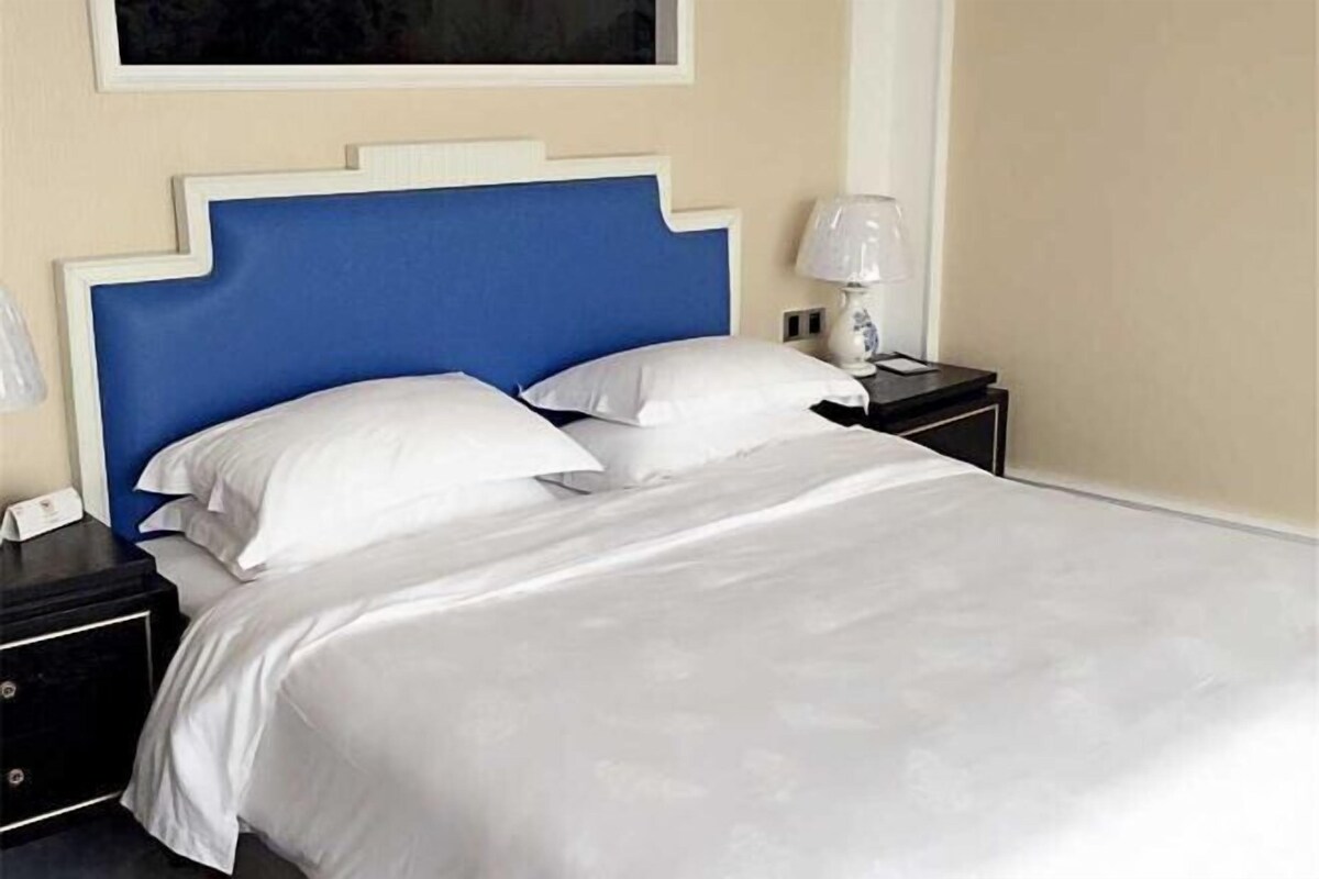 A bed with a blue headboard, white bedding, and a bedside table with a lamp.