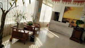 Een woonkamer met een bank, houten stoelen, een bijzettafeltje en een potplant.