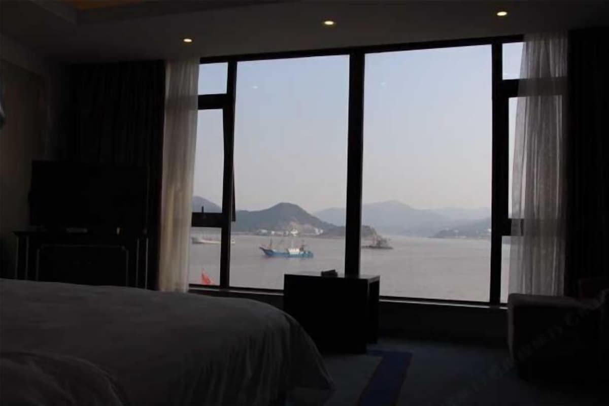 A hotel room with a large window, a bed, a TV, and a desk.