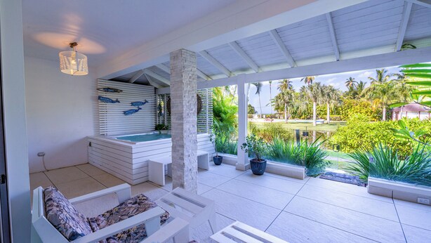 Un espace extérieur aménagé avec des meubles blancs, abrité par une structure, comprenant une piscine et des plantes en pot.