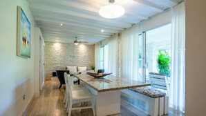 Une cuisine moderne dotée d’un plan de travail en granit, de meubles blancs et d’un coin repas avec des chaises et un banc blancs.