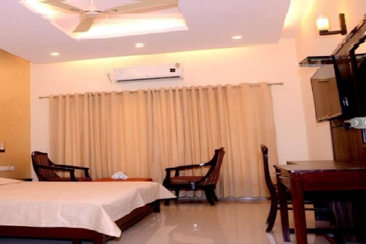 A hotel room with a large bed, two chairs, a desk, and a ceiling fan.