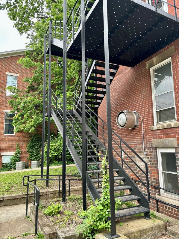Una escalera metálica con techo metálico, que conduce a un edificio de ladrillo con ventanas y un carretel de manguera contra incendios.