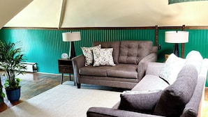 Una sala acogedora con un sofá marrón, un sillón más pequeño y una pared de acento verde.