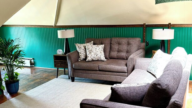 Una sala acogedora con un sofá marrón, un sillón más pequeño y una pared de acento verde.