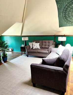 Una sala acogedora con un sofá marrón, un sillón más pequeño y una pared de acento verde.