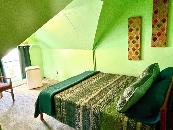 Un pequeño cuarto ático triangular con una cama individual, una silla y una mesita.