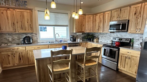 A kitchen with wooden cabinets, a central island with chairs, a microwave, stove, and a refrigerator. - Family friendly, quiet new neighborhood (Missoula)