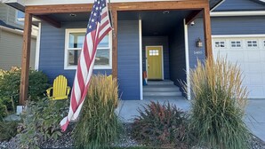 A modern two-story house with a covered front porch, an American flag, and a yellow door. - Family friendly, quiet new neighborhood (Missoula)