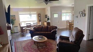 A spacious living room with a brown leather sofa, a leather armchair, and a coffee table. There is a dining area with a table and chairs in the background. - Family friendly, quiet new neighborhood (Missoula)