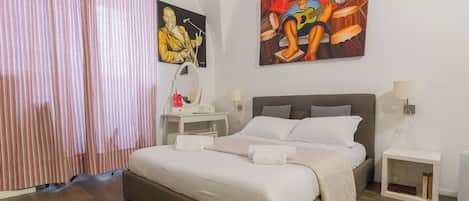 A modern bedroom with a large bed, a desk with a mirror, and two paintings on the wall.