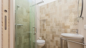 Une salle de bain avec des carreaux décorés, une douche en verre, des toilettes et un lavabo doté d’un support en métal.
