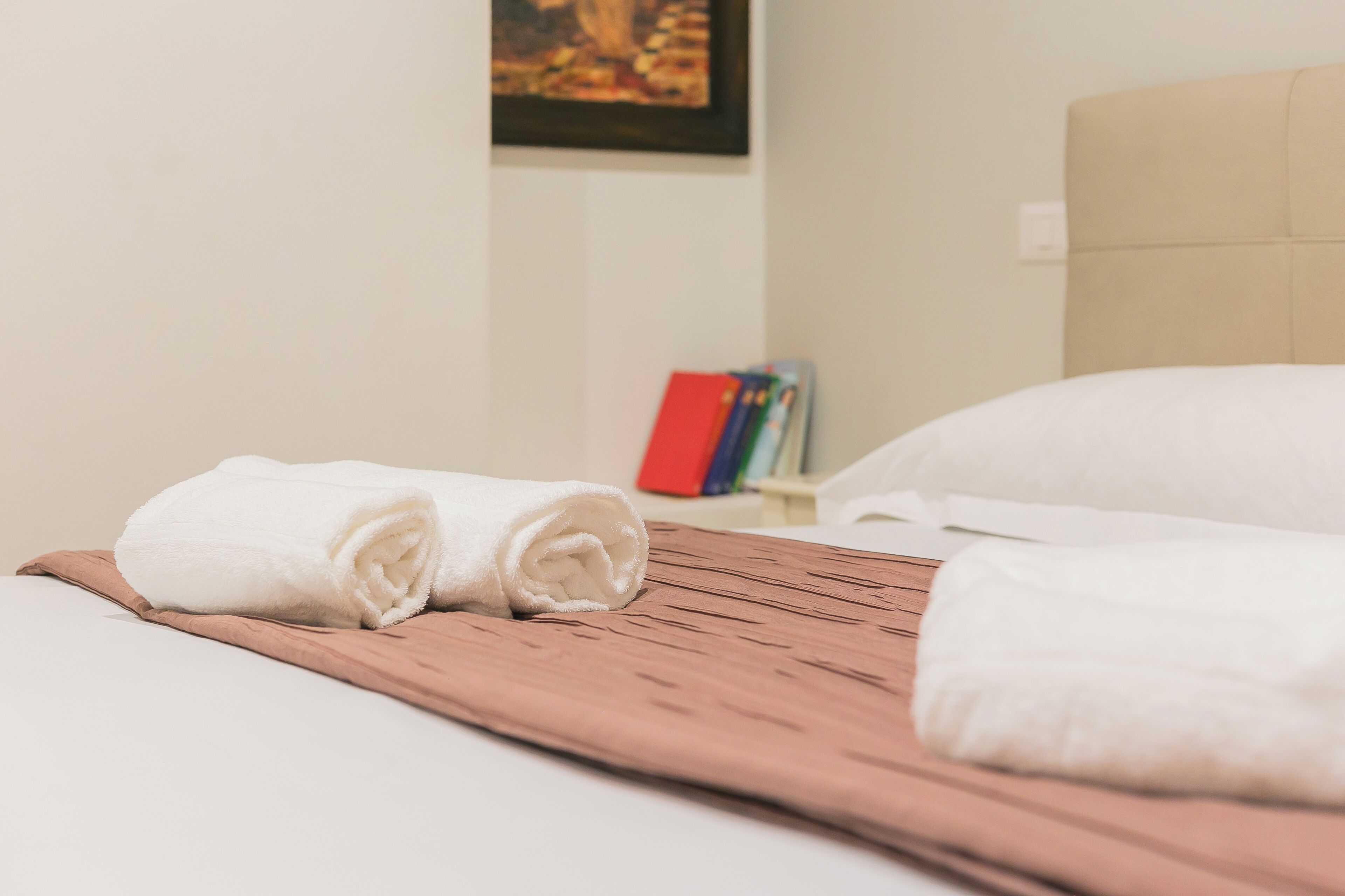 A neatly made bed with a brown blanket and two rolled white towels.