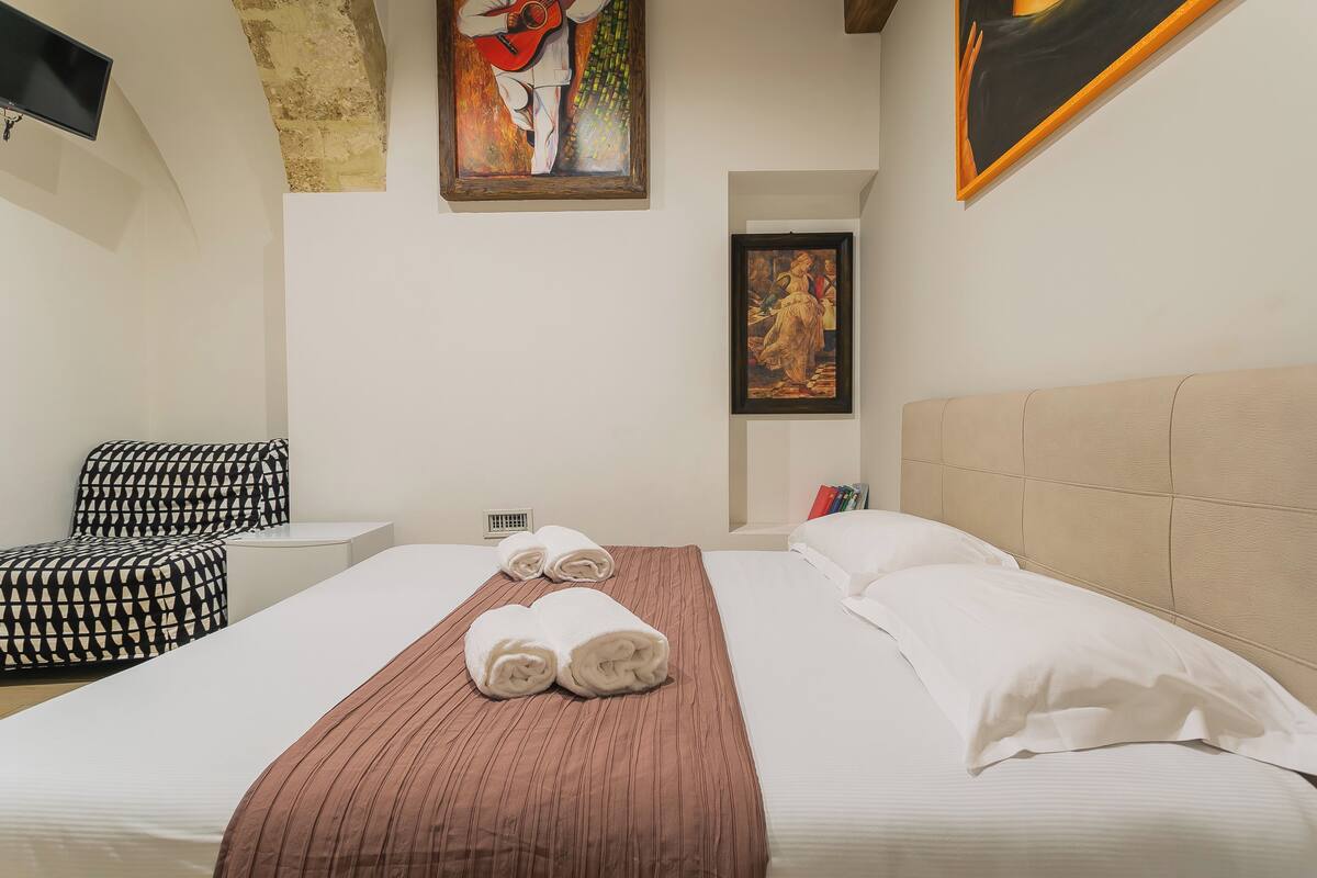 Ein Hotelzimmer mit Bett, Kopfteil, Fernseher und zwei Bildern an der Wand.