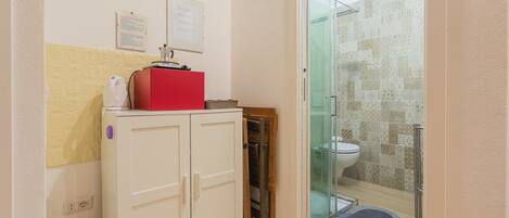 A bathroom with a shower, a toilet, and a white cabinet with a red appliance on top.