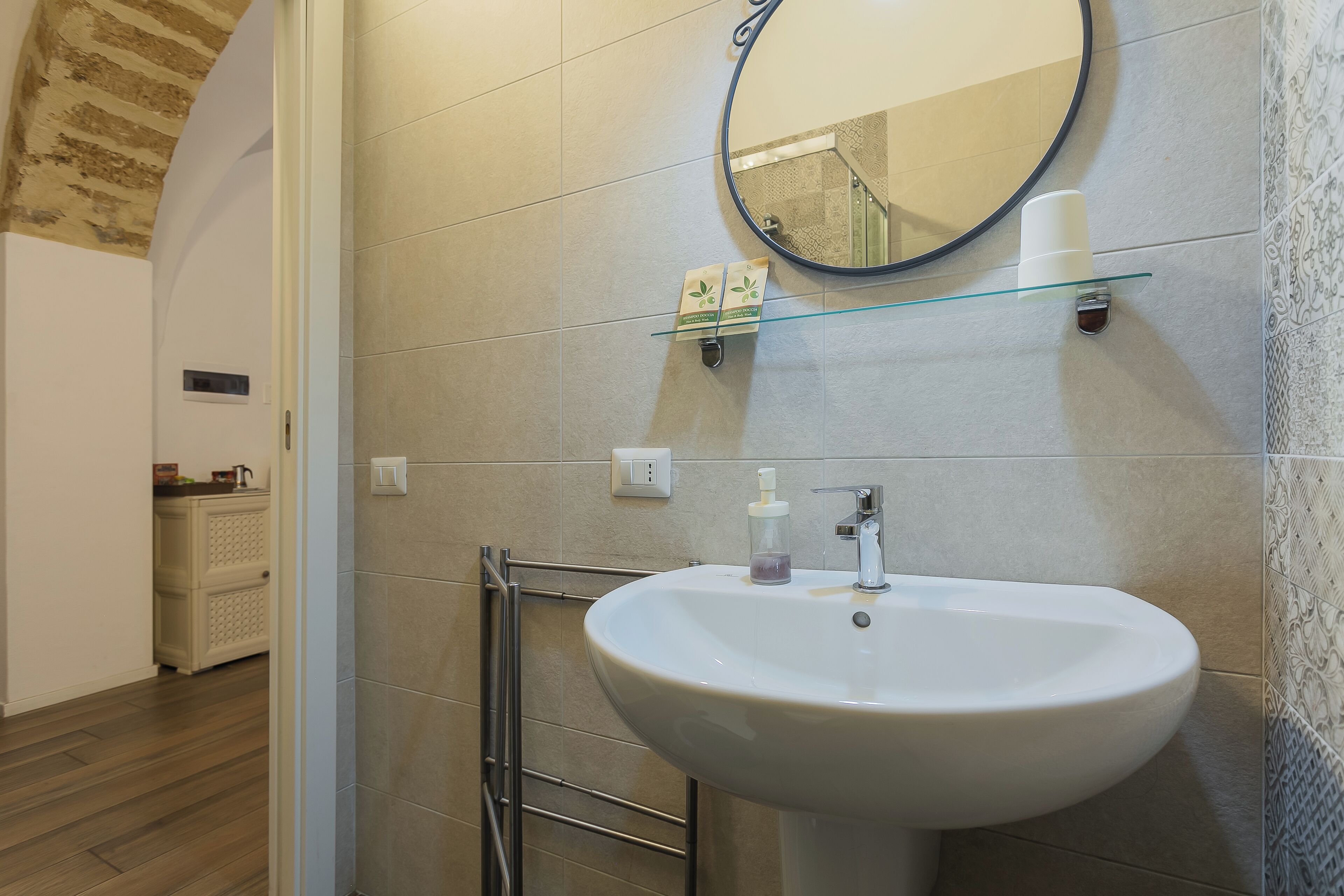 A bathroom with a white sink, a round mirror, and a glass shelf.