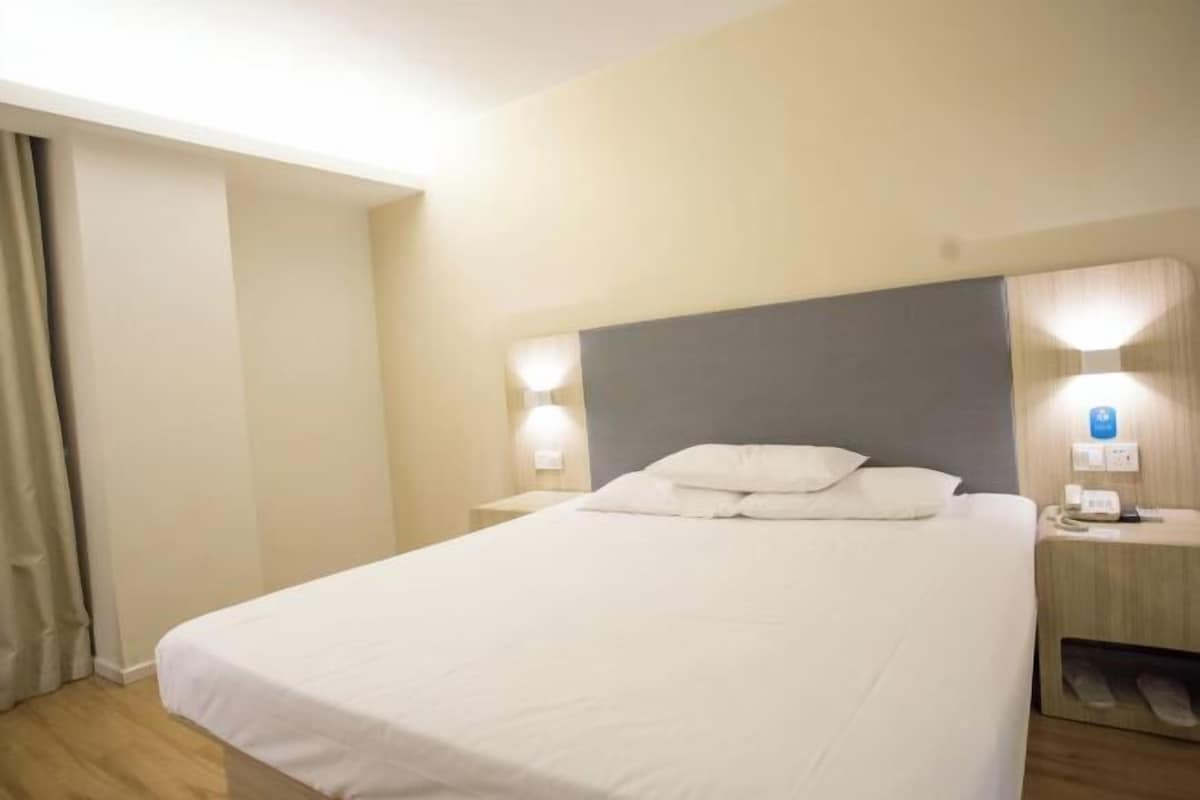 Ett hotellrum med en stor säng, två sängbord, ett litet bord och en telefon som är monterad på väggen.