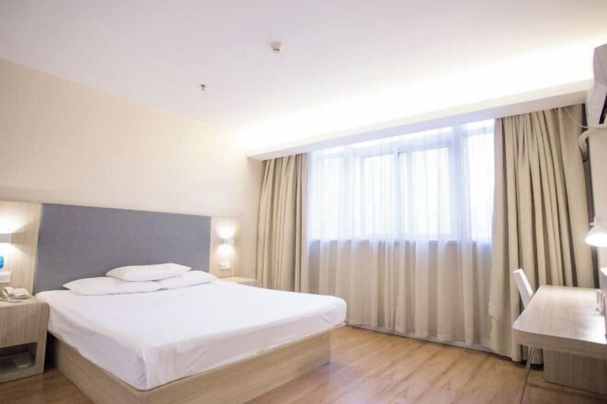 A hotel room with a bed, bedside table, lamp, and a window with curtains.