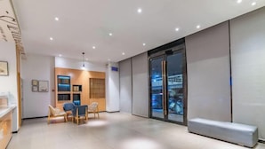 En modern hotellobby med en receptionsdisk, en sittgrupp och ett stort fönster med utsikt över gatan.