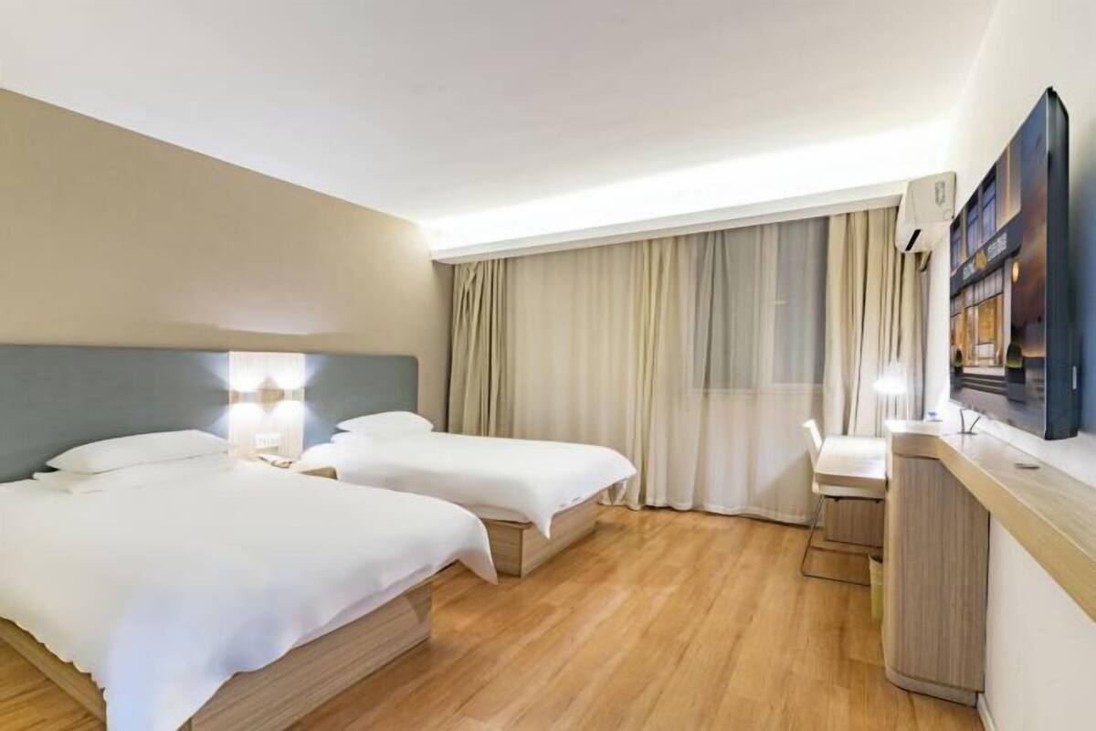 A hotel room with two beds, a desk, a chair, and a TV.