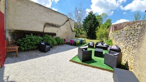 An outdoor seating area with wicker furniture and a table, surrounded by a gravel path and greenery. - Sweet Home (Bélâbre)