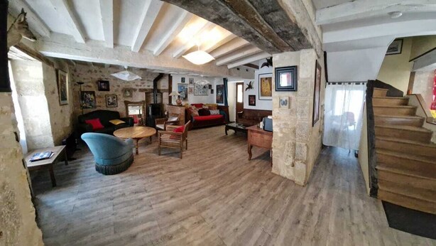 A rustic room with exposed wooden beams, a stone wall, a wooden staircase, and a mix of furniture including a blue armchair, a red sofa, and a wooden coffee table. - Sweet Home (Bélâbre)