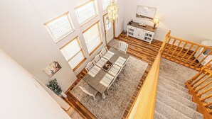 Ein geräumiger Essbereich mit Holztisch und Stühlen, einer Chandelieber und Blick auf die Küche und die Treppe.