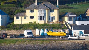 A coastal house with a driveway, a yellow boat, and a white van parked nearby.