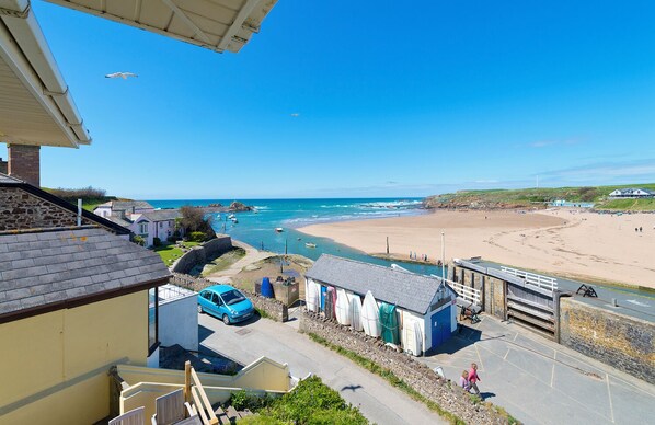 Une ville côtière avec une plage de sable, un mur de pierre et une voiture bleue garée dans la rue.