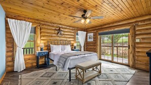 Ein Schlafzimmer in einer Blockhütte mit Bett, Sitzbank, Deckenventilator und großem Fenster.