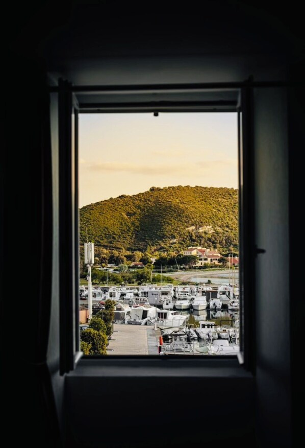 A view from a window overlooking a marina with boats, a hilly landscape, and buildings in the background.
