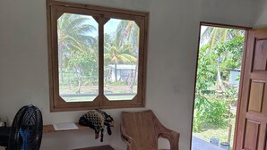 A bedroom with a bed, a chair, a fan, a window, and a door.