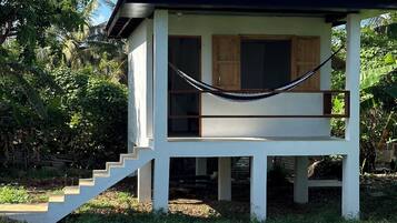 Guest house surrounded by lush greenery, featuring a wooden staircase and hammock.