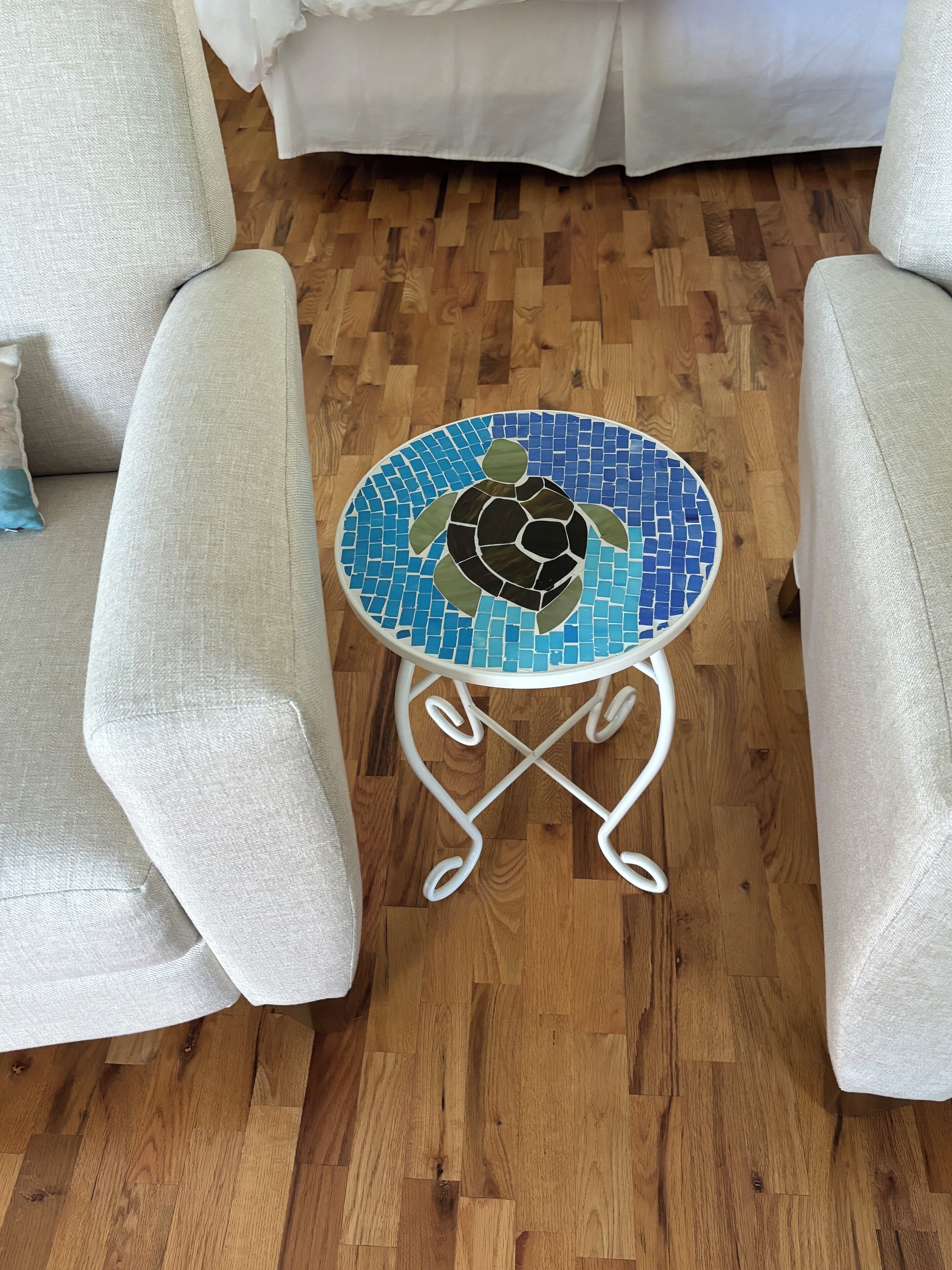 A round table with a mosaic turtle design on a wooden floor, surrounded by two beige armchairs.