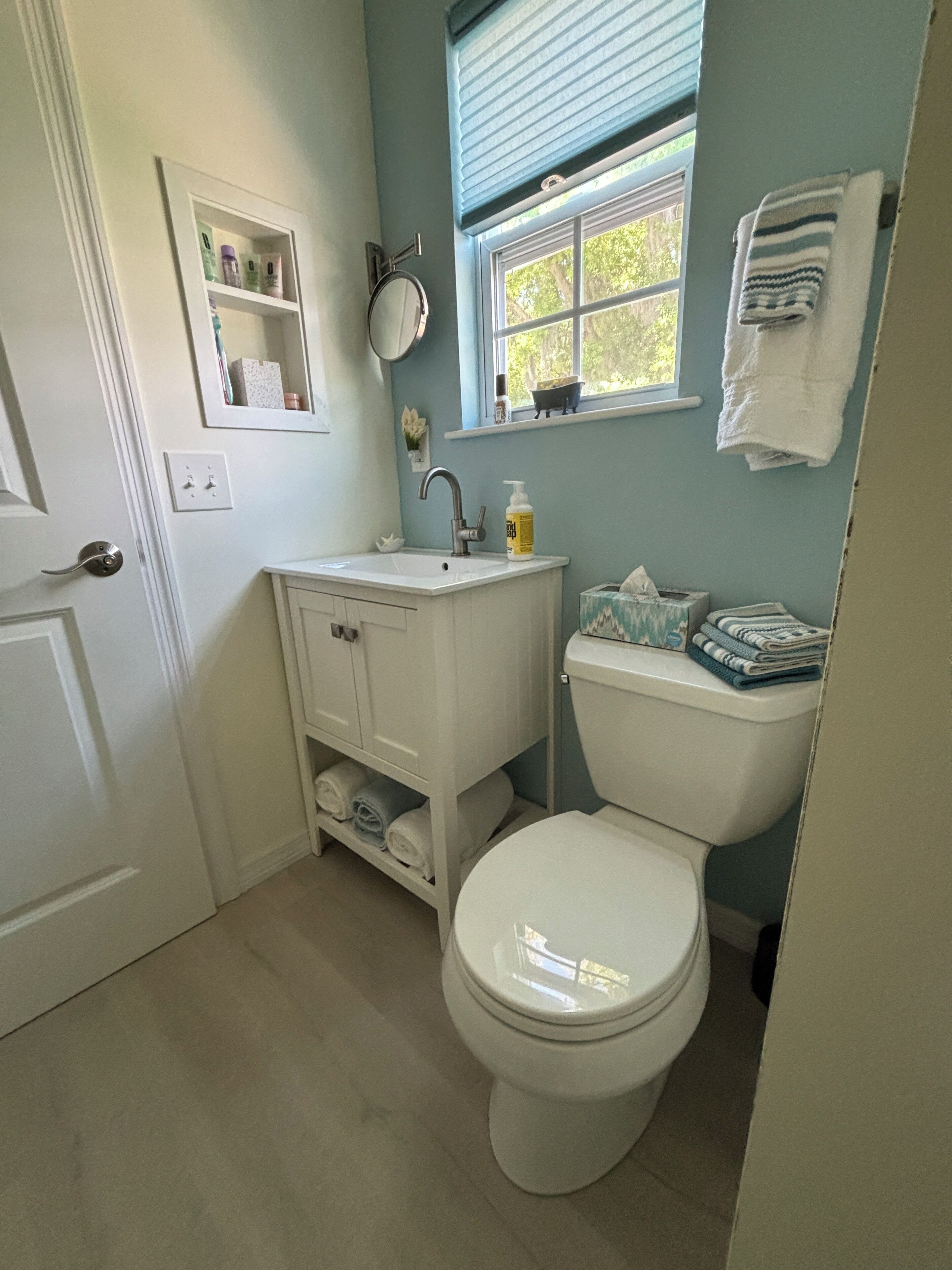Un baño con inodoro blanco, lavabo con espejo y ventana con toalla colgada en la pared.