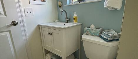 Un baño con inodoro blanco, lavabo con espejo y ventana con toalla colgada en la pared.