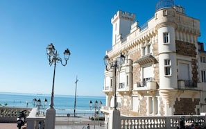 Um edifício à beira-mar com varanda, postes de iluminação e vista clara do oceano.