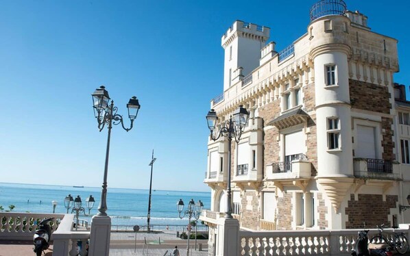 A seaside building with a balcony, street lamps, and a clear view of the ocean.